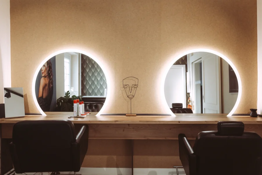 Professioneller Friseursalon mit zwei beleuchteten ovalen Spiegeln, Holzoberflächen und zwei schwarzen Ledersitzen, ideal für Imagefotos von Unternehmen.