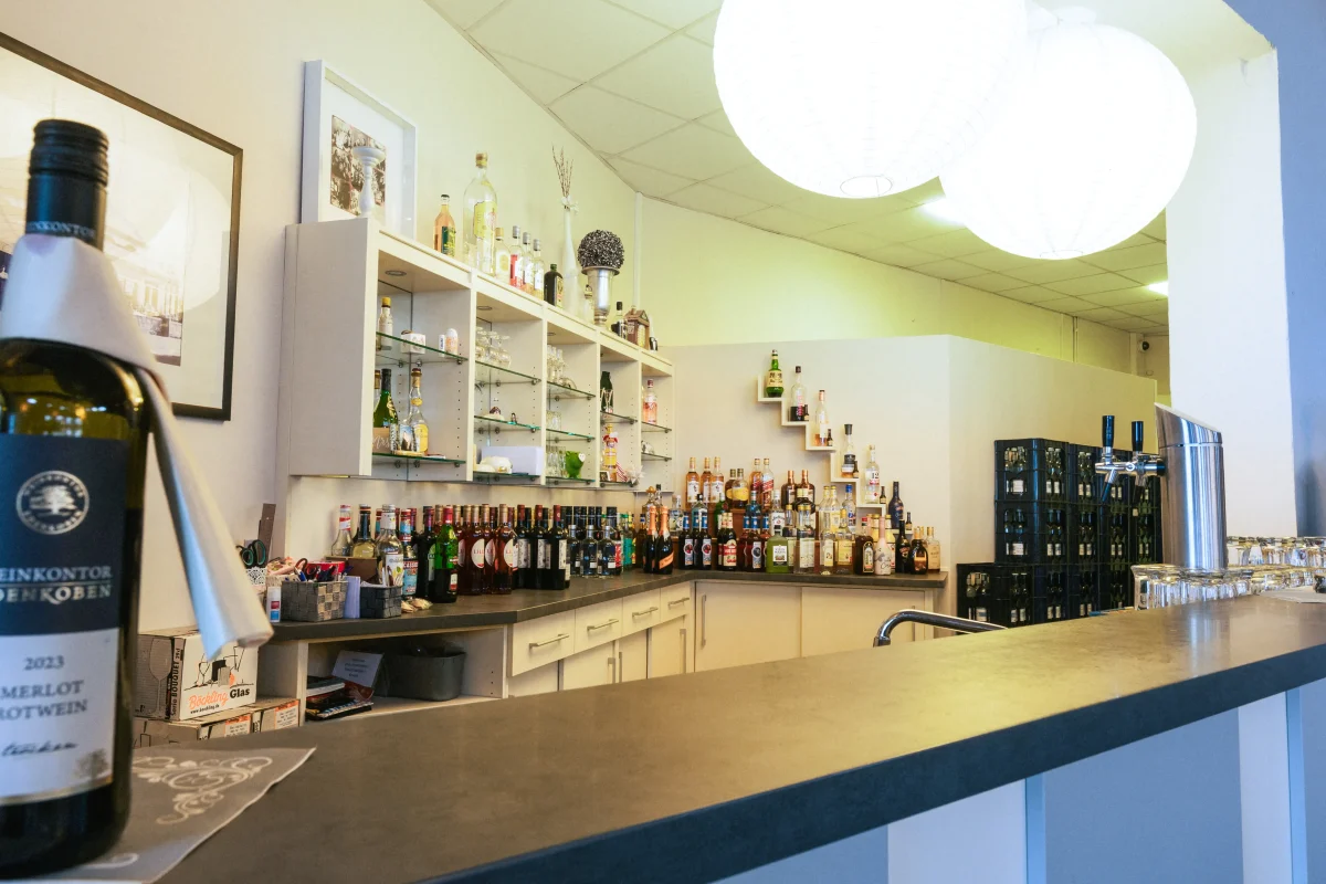 Eine Weinbar mit Regalen voller Flaschen, Zapfanlagen und Gläsern, beleuchtet von modernen Lampen. Ein Weinlabel mit der Aufschrift 