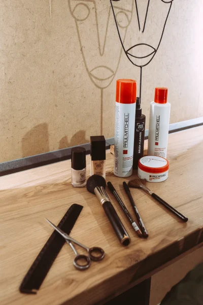 Professionelle Make-up-Pinsel, Schere und Haarpflegeprodukte von Paul Mitchell auf einer Holzoberfläche, ideal für Unternehmen, die einen Fotografen und Imagevideografen suchen.