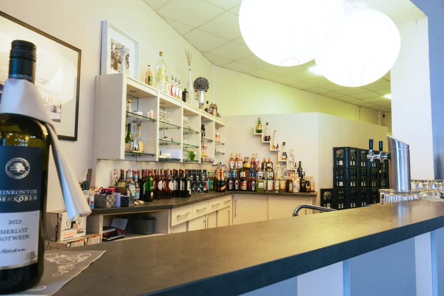Eine Weinbar mit Regalen voller Flaschen, Zapfanlagen und Gläsern, beleuchtet von modernen Lampen. Ein Weinlabel mit der Aufschrift 