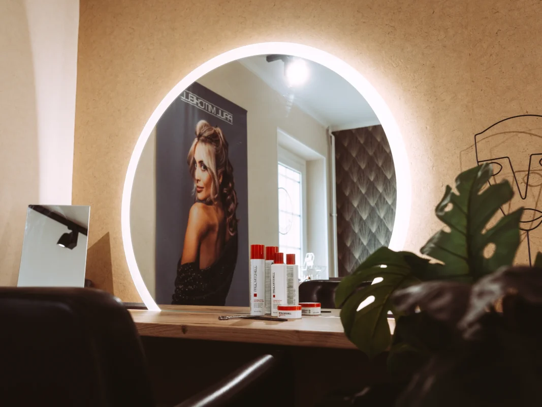 Ein moderner Friseursalon mit einem beleuchteten, runden Spiegel, der ein Paul Mitchell Werbeposter reflektiert. Als spezialisierter Unternehmen Fotograf und Imagevideograf setze ich solche professionellen Arbeitsumgebungen ästhetisch in Szene.